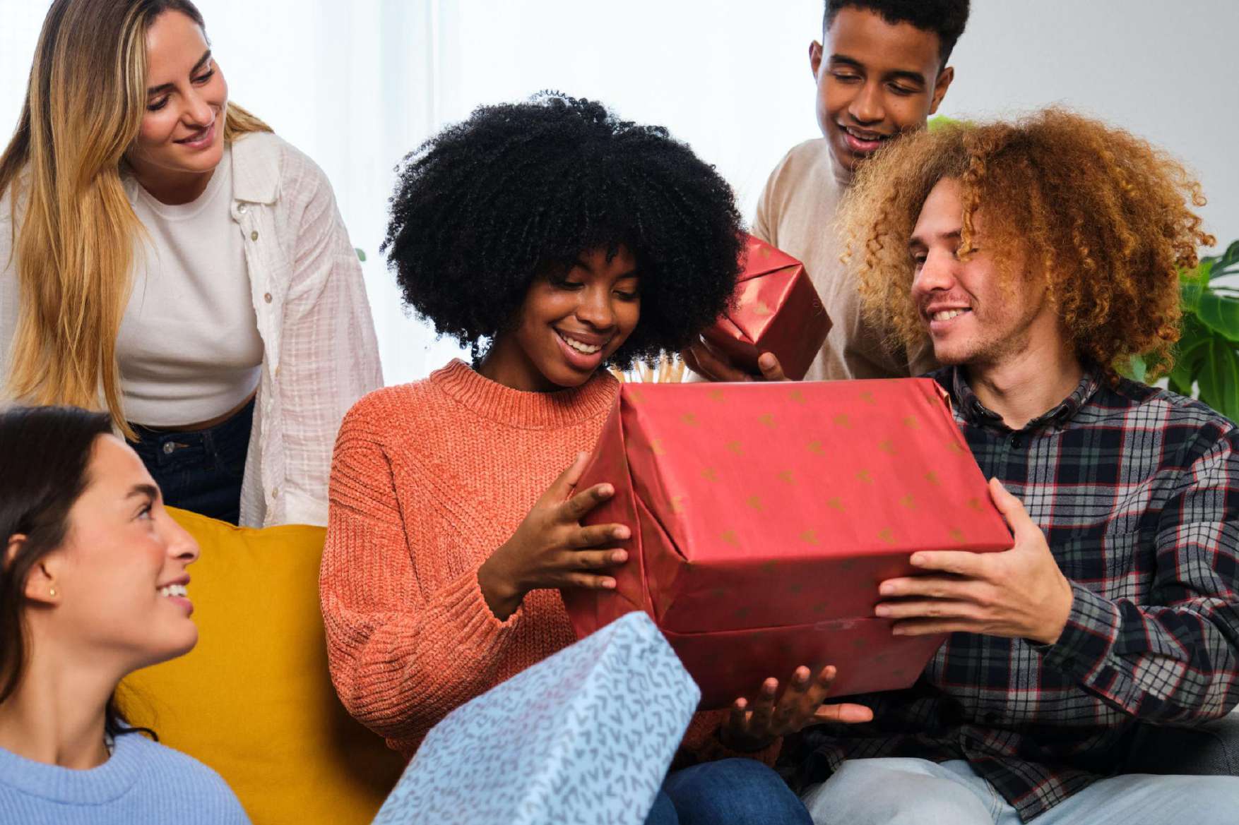 Friends leaning in as a woman opens a red gift