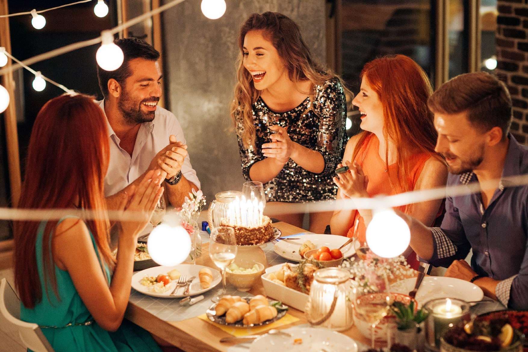 Friends around a birthday cake with candles under string lights